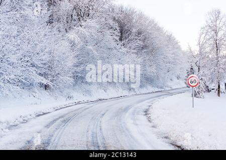 Piste da neve su una strada di campagna e cartelli a 60 km/mph. Foto Stock