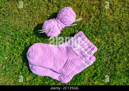 Un paio di belle calze di lana di cotone per un bambino o per un regalo fatto a mano. Un set di aghi da maglieria e filo di lana rosa su sfondo verde erba. Foto Stock