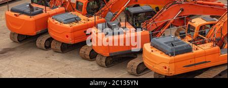 Vecchi escavatori pesanti arancioni parcheggiati in una fila su una superficie in cemento. Cantiere. Vista aerea angolata. Foto Stock