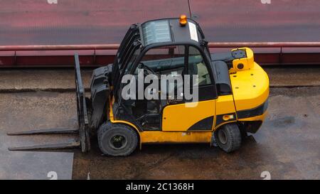 Carrello giallo parcheggiato su una superficie di cemento bagnata. Sito industriale. Foto Stock