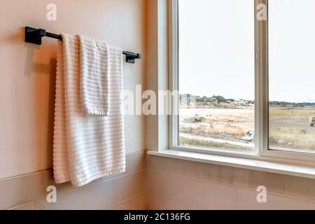 Asciugamano bianco appeso su asta nera montato sulla parete del bagno con piastrelle Foto Stock