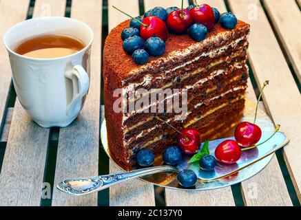 Torta al miele con cioccolato a fette di noce, prugne, panna acida, guarnita con ciliegie e aronia Foto Stock