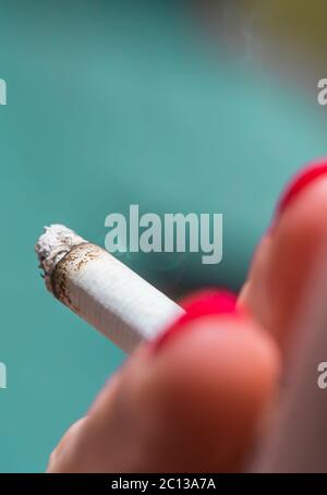 Una donna con chiodi rossi dipinti che fuma una sigaretta all'esterno. Foto Stock