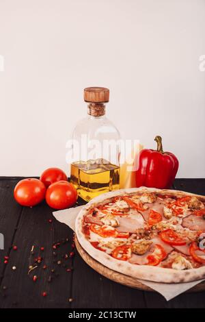 Gustosa pizza italiana e ingredienti per cucinare pomodori, erbe, formaggio su fondo nero di cemento. Pizza con pancetta calda. Foto Stock