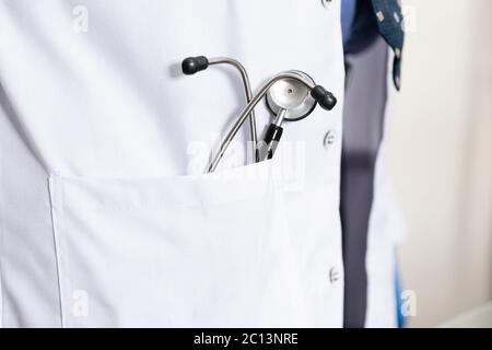 Primo piano di stetoscopio in un cappotto medico, guanti blu. Telescopio in tasca Foto Stock