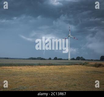 un fulmine colpisce il terreno accanto a una turbina eolica Foto Stock