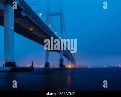 Vista del ponte della baia di Yokohama dal Daikoku Pier West Park durante l'ora blu prima dell'alba sotto il cielo piovoso e nuvoloso. Foto Stock