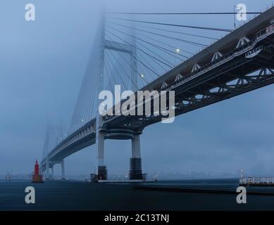 Vista del ponte della baia di Yokohama dal Daikoku Pier West Park durante l'ora blu prima dell'alba sotto il cielo piovoso e nuvoloso. Foto Stock