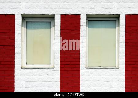 struttura di muro in mattoni rosso luminoso con strisce bianche e finestre in una giornata di sole. Foto Stock