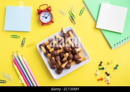 Forniture scolastiche e biscotti per uno spuntino sul tavolo giallo con spazio di copia. Scuola di concetto, Foto Stock