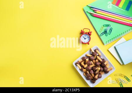 Forniture scolastiche e biscotti per uno spuntino sul tavolo giallo con spazio di copia. Scuola di concetto, Foto Stock