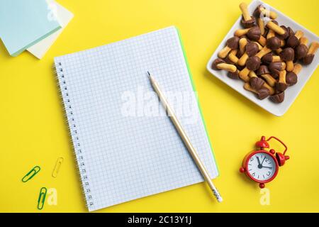 Forniture scolastiche e biscotti per uno spuntino sul tavolo giallo con spazio di copia. Scuola di concetto, Foto Stock