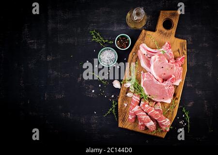 Bistecche di maiale crudo. оn diversi tipi di carne di maiale cruda e di salsicce tritate sono da tavola scura. Vista dall'alto, dall'alto, spazio per la copia Foto Stock