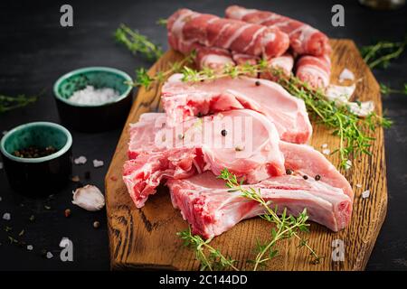 Bistecche di maiale crudo. оn diversi tipi di carne di maiale cruda e di salsicce tritate sono da tavola scura. Spazio di copia Foto Stock