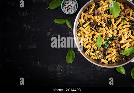 Fusilli con spinaci e funghi in padella. Cibo vegetariano / vegano. Cucina italiana. Vista dall'alto, disposizione piatta, spazio per la copia Foto Stock