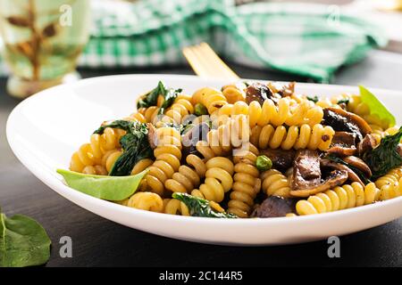 Fusilli con spinaci e funghi su un piatto bianco. Cibo vegetariano / vegano. Cucina italiana. Foto Stock