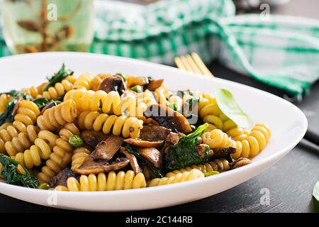 Fusilli con spinaci e funghi su un piatto bianco. Cibo vegetariano / vegano. Cucina italiana. Foto Stock