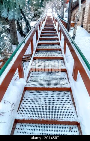 Concentratevi sulle scale con gradini a griglia e corrimano in metallo contro la collina coperta di neve Foto Stock