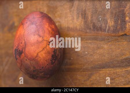 Uovo di Pasqua su sfondo di legno. Verniciato marrone con macchie e crepe. Primo piano macro con copyspace Foto Stock