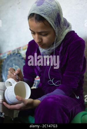 Una ragazza marocchina con un velo dipinge una ciotola in una fabbrica di ceramica a Fes, Marocco Foto Stock