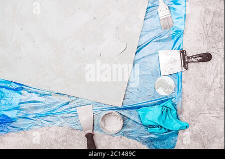 Tavola intonacata, spatola in metallo, vasetto di cemento, pennello per vernice molare, panno blu e un rivestimento pavimento in telofano blu. Autoriparazione e arredamento, buildi Foto Stock