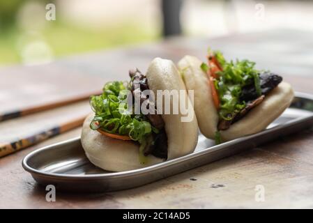 due bao asiatici farciti con verdure alla lattuga e pancia di maiale su un tavolo di legno e bastoncini di pollo Foto Stock