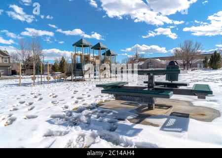 Parco giochi e tavolo da picnic con impronte sul terreno innevato in inverno Foto Stock