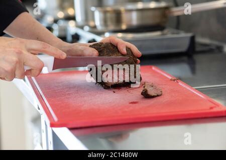 taglio a mano di fette di pastrami sul tagliere facendo una ricetta Foto Stock