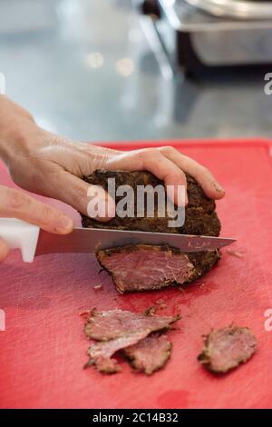 taglio a mano di fette di pastrami sul tagliere facendo una ricetta Foto Stock