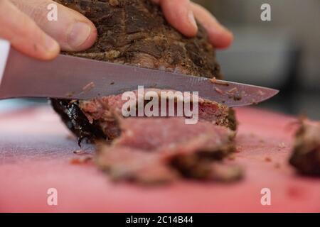 taglio a mano di fette di pastrami sul tagliere facendo una ricetta Foto Stock