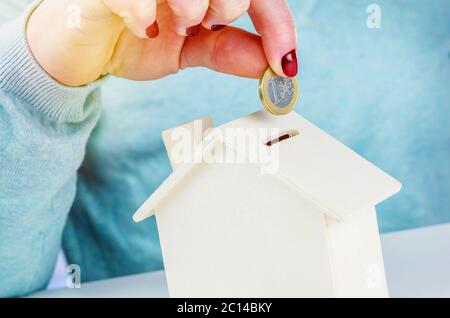 Donna che inserisce una moneta in euro in una cassa di denaro di legno Foto Stock