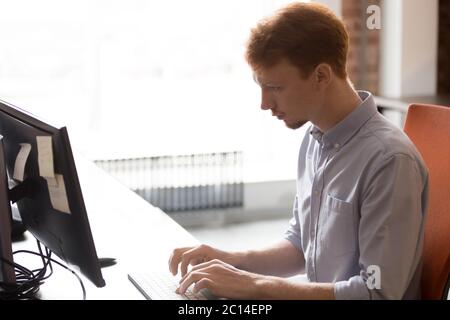 Un dipendente serio che lavora per affari usa il computer, seduto sul posto di lavoro Foto Stock