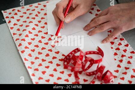 Una donna con sta lavorando con un righello di cucitura, prepara i materiali di fabbricazione della maschera a casa con il pattern del cuore durante COVID-19. Fision, laboratorio di sarto. Foto Stock