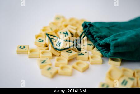 Piastrelle di lettera di gioco di Scrabble casuali con valore di punteggio che esce dalla loro borsa verde di stringa di disegno. Quarantena home entertainmentin per Coronavirus indossare Foto Stock