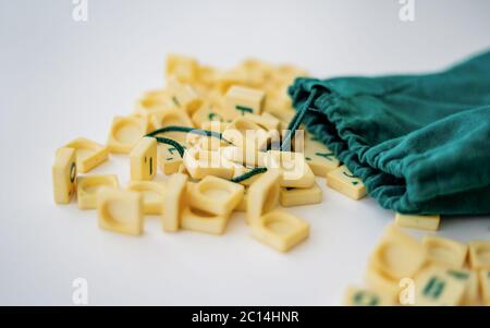 Piastrelle di lettera di gioco di Scrabble casuali con valore di punteggio che esce dalla loro borsa verde di stringa di disegno. Quarantena home entertainmentin per Coronavirus indossare Foto Stock