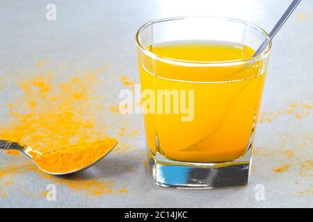 Acqua curcuma in una tazza di vetro e polvere curcuma in un cucchiaino Foto Stock