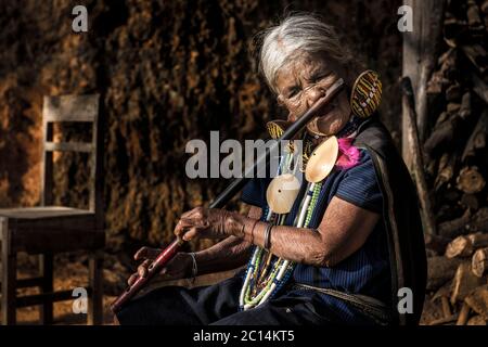 Yaw Shen, una donna matura K'cho Chin con tatuaggi viso, suona flauto naso tradizionale, Chin state, Myanmar Foto Stock