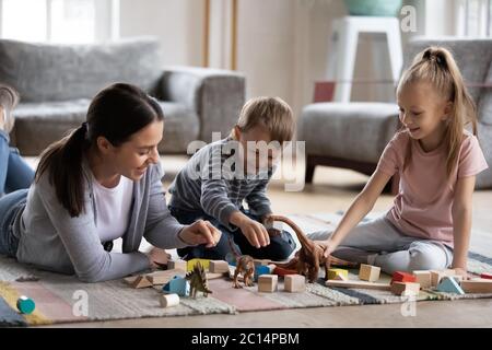 Felice madre che gioca con adorabile figlia e figlio sul pavimento Foto Stock