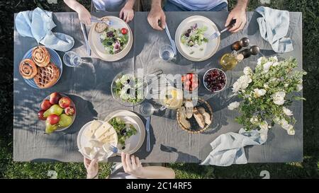 Cena per famiglie all'aperto. Cena in famiglia con insalata biologica e formaggio su un tavolo alla moda in stile scandinavo in giardino. Sano estetica cibo bello, concetto di staycation estivo. Vista aerea o dall'alto Foto Stock