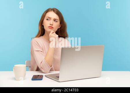 Deve pensare al piano di affari. Donna penosa in abiti casual seduta con espressione ponderata e confuso mentre si lavora su un computer portatile in ufficio a casa. Foto Stock