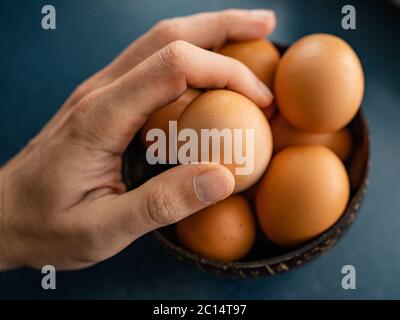 Persona che sceglie l'uovo migliore dal recipiente delle uova grezze di pollo sullo sfondo di legno. Spazio per il testo Foto Stock