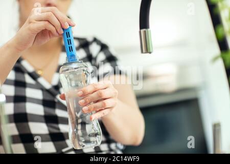 Inserimento del filtro al carbonio nella bottiglia. Donna inserisce il filtro al carbonio nella bottiglia riutilizzabile con acqua fresca in cucina. Vista frontale. Foto Stock