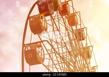 Ruota panoramica con cabine multicolore contro il cielo con nuvole e raggi solari nel parco in una soleggiata giornata primaverile. Foto Stock