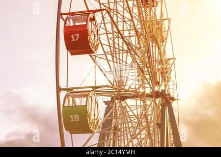 Ruota panoramica con cabine multicolore contro il cielo con nuvole e raggi solari nel parco in una soleggiata giornata primaverile. Foto Stock