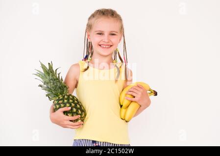 Carino beatiful bambina con capelli intrecciati che tengono banana e ananas, su sfondo bianco Foto Stock