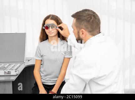 Medico oftalmologo che tiene l'attrezzatura speciale dell'occhio che esamina gli occhi della ragazza adolescente nella clinica Foto Stock
