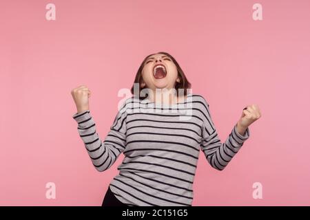 Vittoria trionfale! Ritratto di donna estremamente felice, sopravorato in felpa a righe gridando per gioia con pugni rialzati, celebrando il successo, euforia Foto Stock