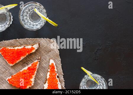 Panini con caviale rosso e un bicchiere di vodka su sfondo nero con spazio per il testo Foto Stock