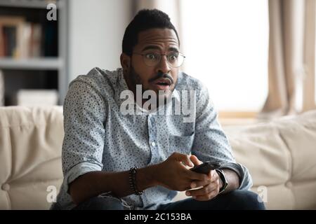 Un ragazzo africano che tiene il telecomando guardando un film si sente spaventoso Foto Stock