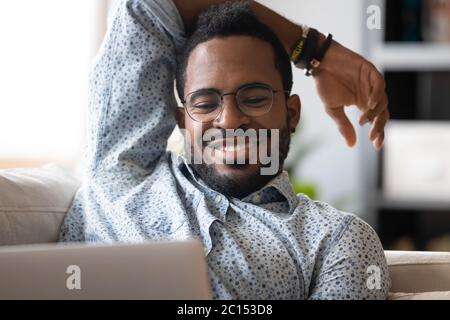 Un collega africano che riposa sul divano usando il computer che guarda il film Foto Stock